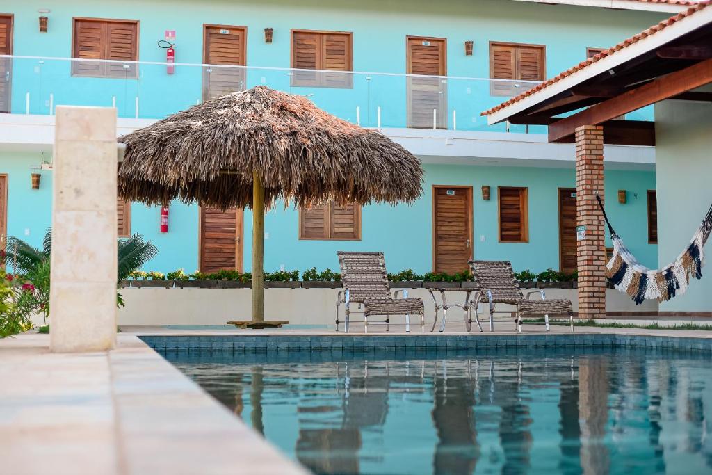 um resort com uma piscina com cadeiras e um guarda-sol de palha em Pousada Maanain em Icapuí