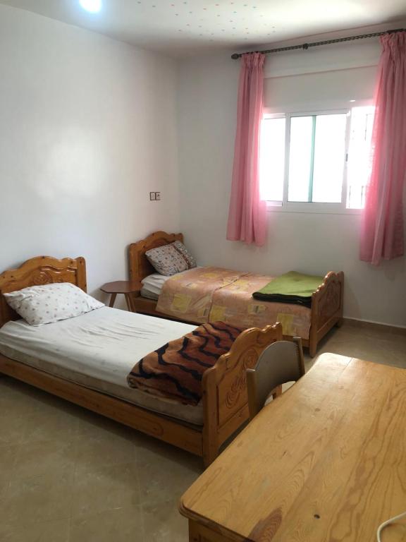 a bedroom with two beds and a table and a window at Vittel Ifrane Large and Beautiful Apartment in Ifrane