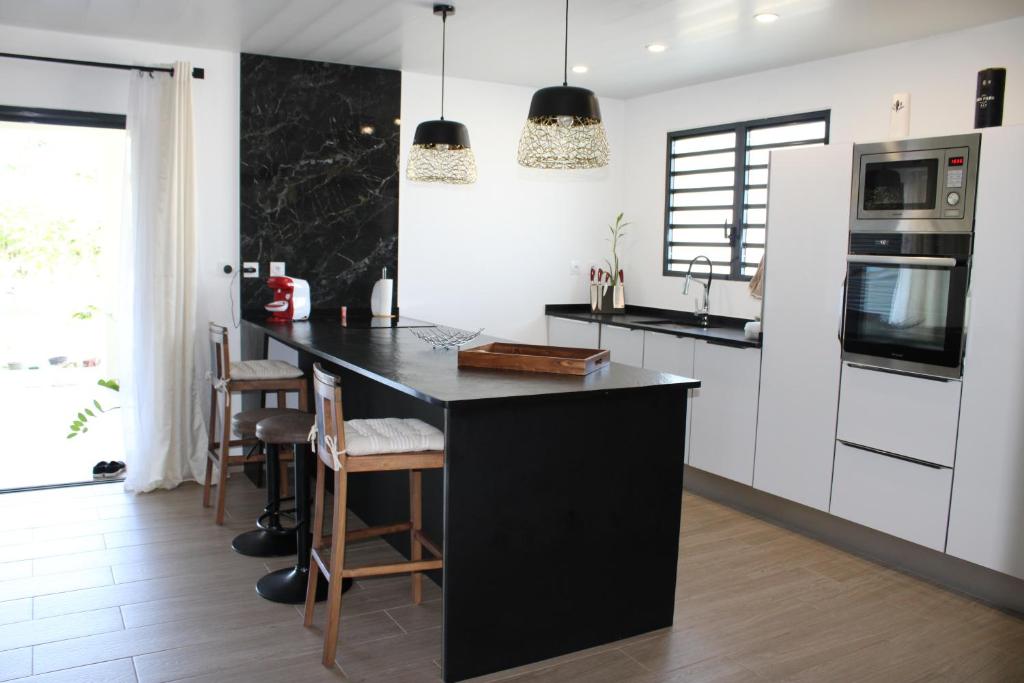 une cuisine avec un îlot noir et des armoires blanches dans l'établissement Villa Perle - 2 suites, à Matoury