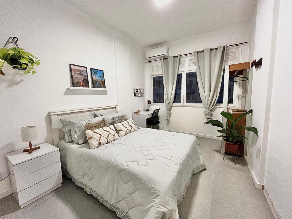 a white bedroom with a white bed and windows at Apartamento praia de Copacabana in Rio de Janeiro