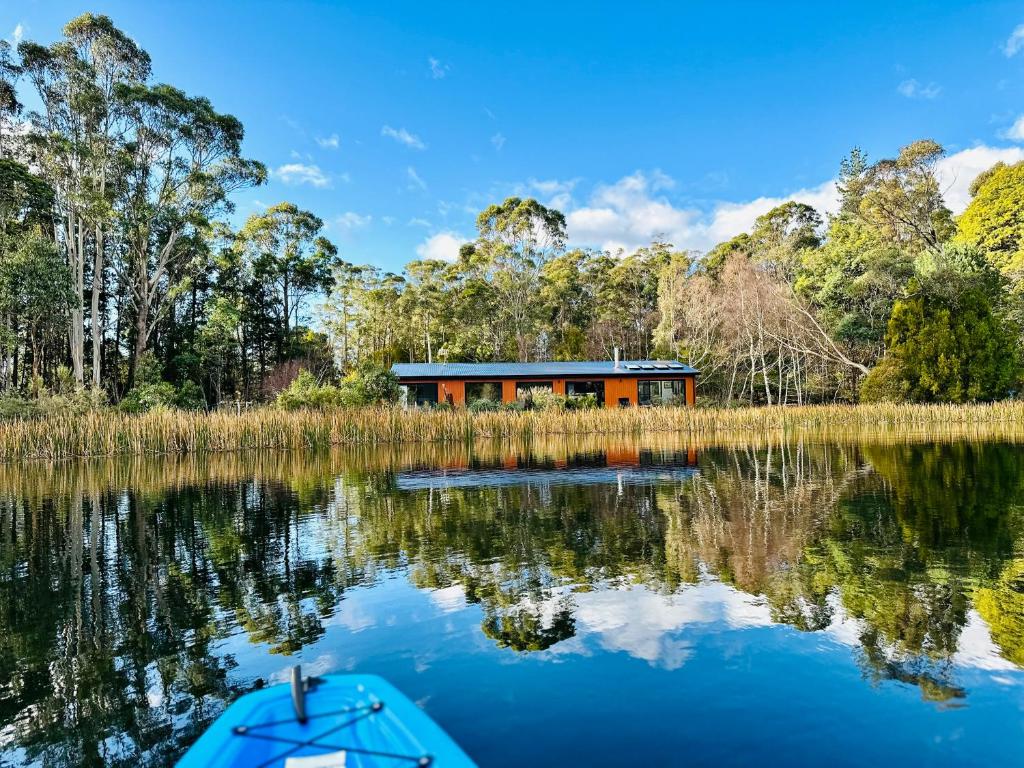 a house on the water with a boat in front of it at Quamby Bluff Lake House, Deloraine, Tasmania in Golden Valley