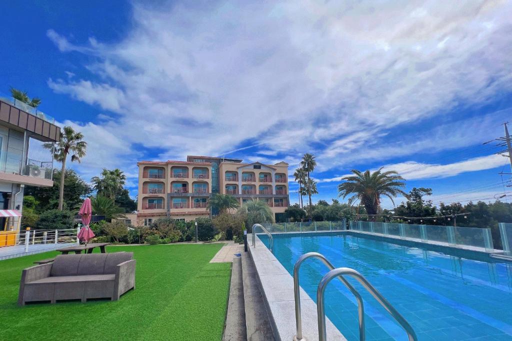 a large swimming pool with green grass next to a building at The Bay Jeju Resort in Seogwipo