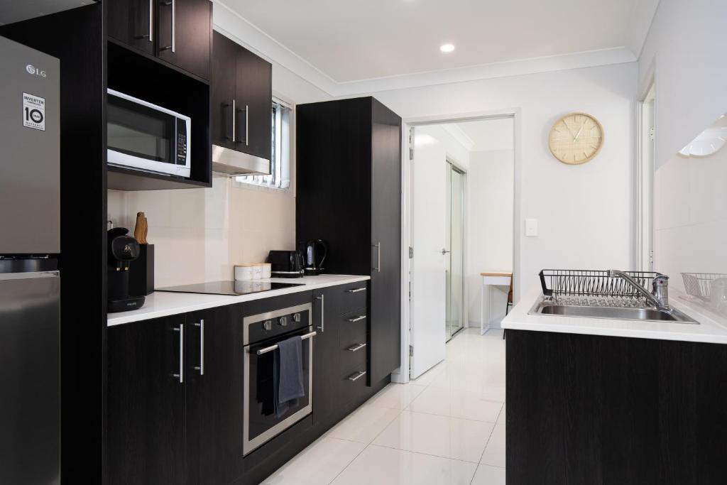 a kitchen with black cabinets and a clock on the wall at Neatly Presented,Air Con and Modern! in Brisbane