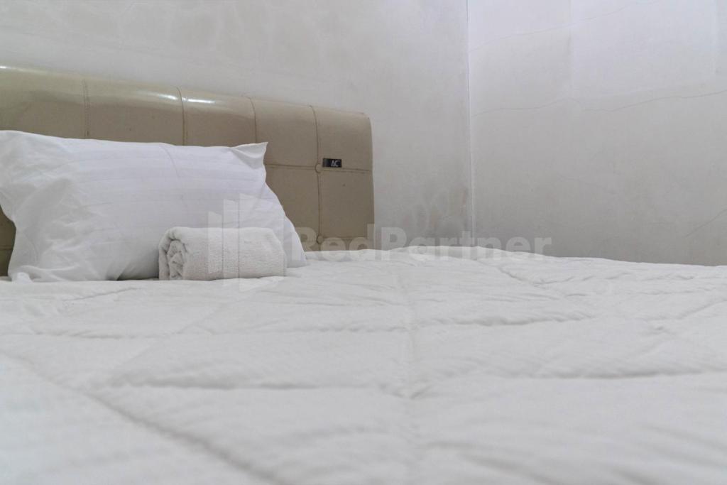 een wit bed met witte lakens en kussens bij Asri Residence near Jalan Iskandar Muda Medan RedPartner in Medan
