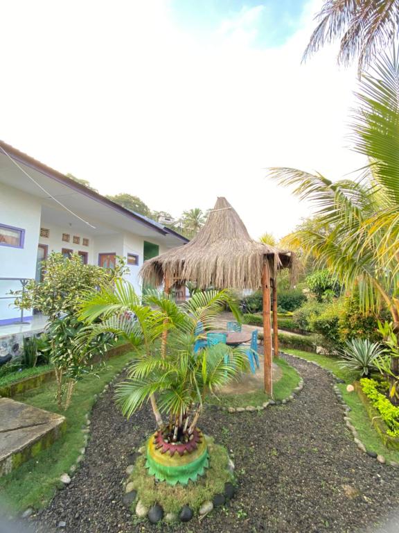a garden with a umbrella and a palm tree at Mahoni Guest House in Kelimutu