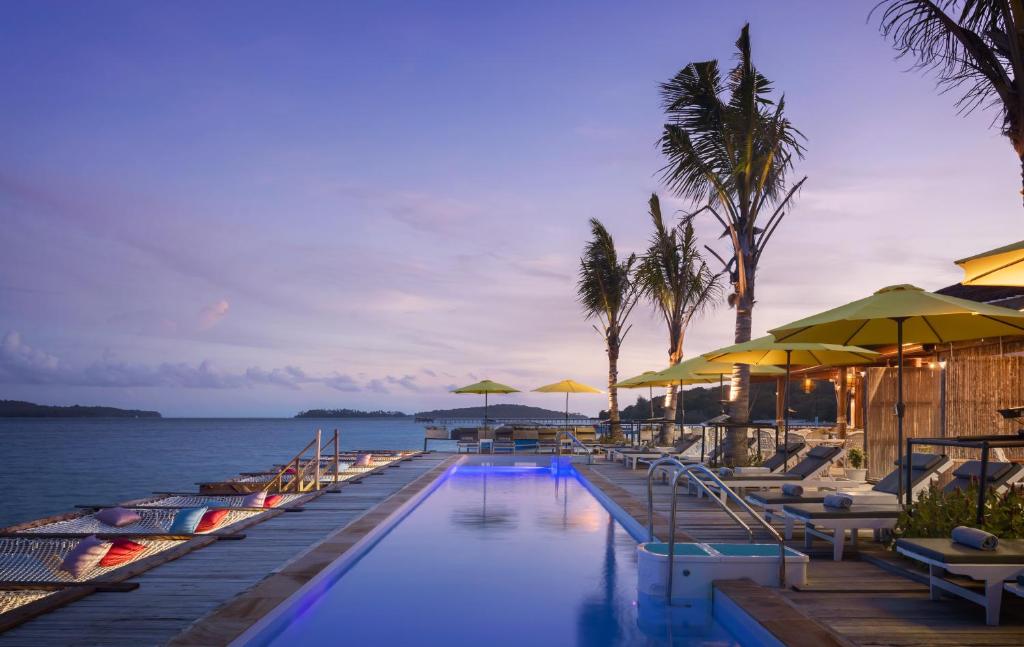 a swimming pool with chairs and umbrellas and the ocean at Koh Apikjun Resort in Kaoh Sdach