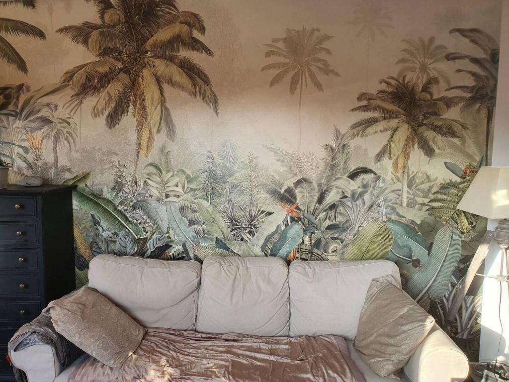 a couch in a living room with a mural of palm trees at Le Vallis Curans in Saint-Raphaël