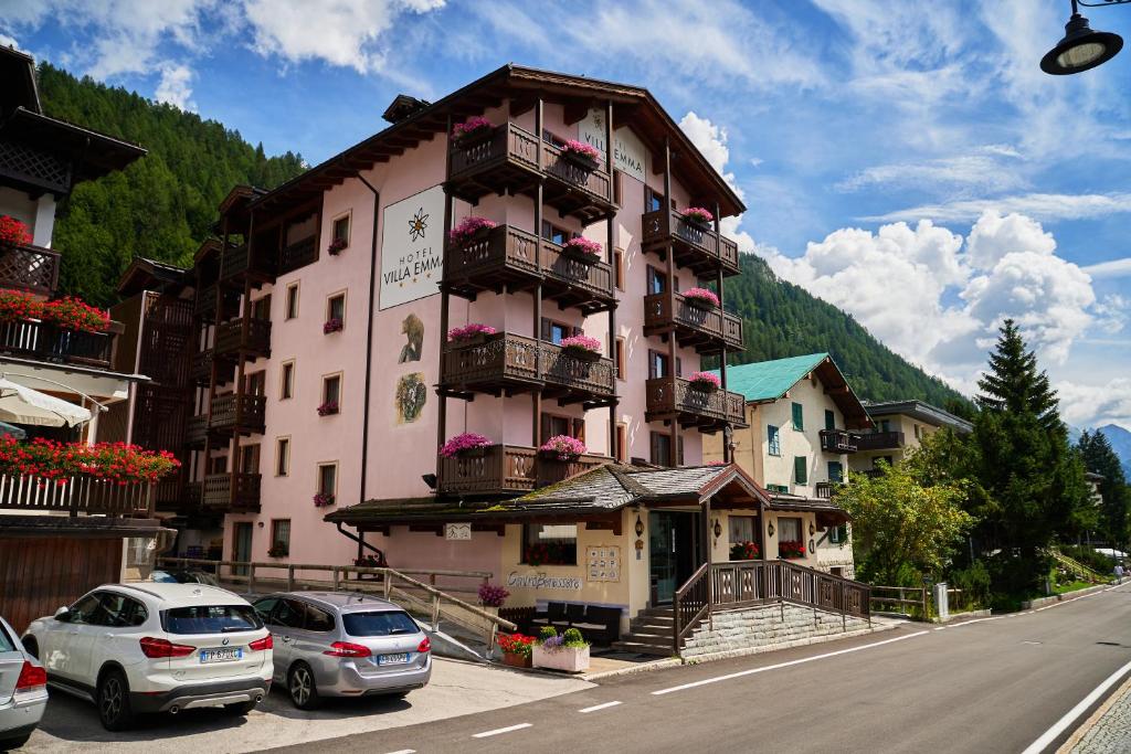 różowy budynek z samochodami zaparkowanymi przed nim w obiekcie Hotel Villa Emma w Madonna di Campiglio