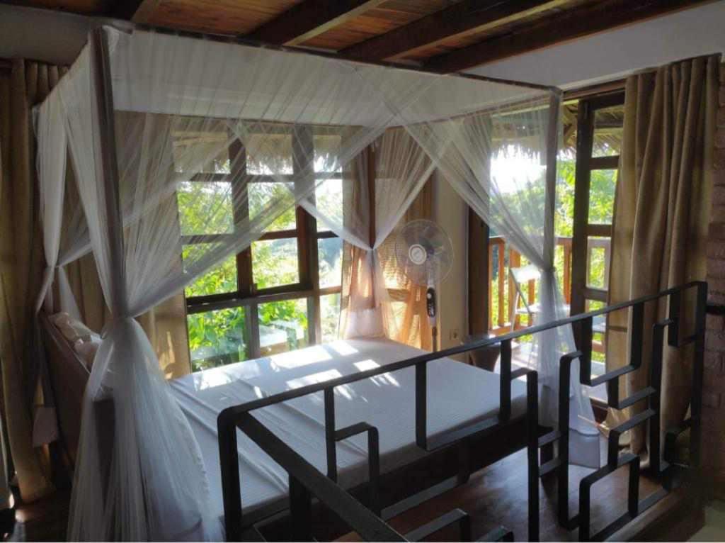 a bedroom with a canopy bed and a window at Moemoea Lodge in Ambatoloaka