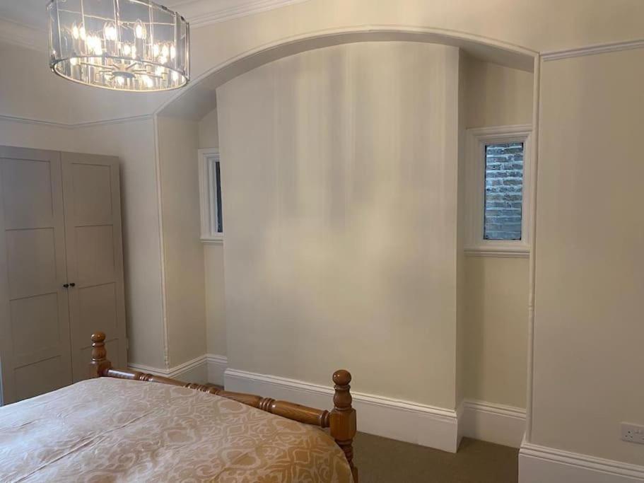 a bedroom with a bed and a window and a chandelier at Beautiful ground floor flat in London