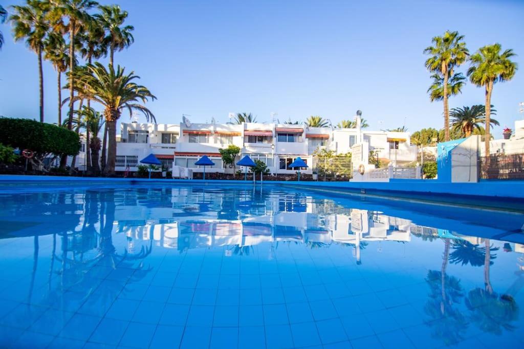 a swimming pool with palm trees and buildings at Chaparal Design Apartment in Costa Del Silencio