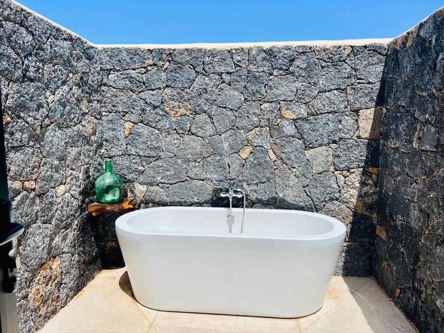 a white bath tub in a bathroom with a stone wall at Villa Lavayarena in La Oliva