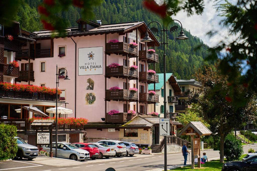 duży różowy budynek z samochodami zaparkowanymi na parkingu w obiekcie Hotel Villa Emma w Madonna di Campiglio