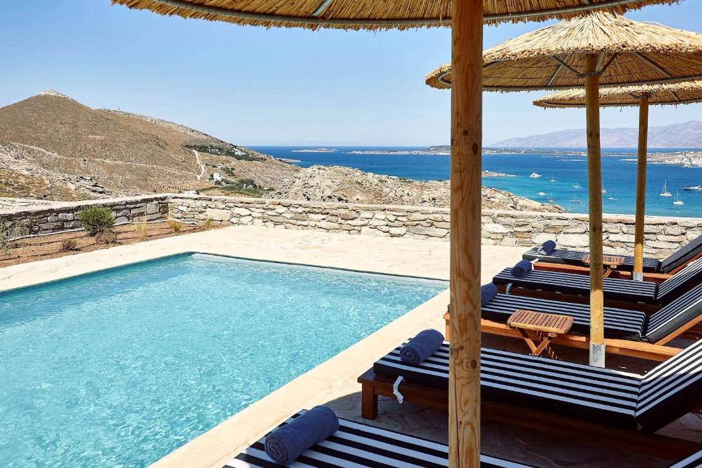 a swimming pool with chairs and an umbrella and the ocean at Platinum Paros Villa - 2 Bedrooms - Villa Turquoise - Sea View & Private Pool - Naoussa in Kolympithres