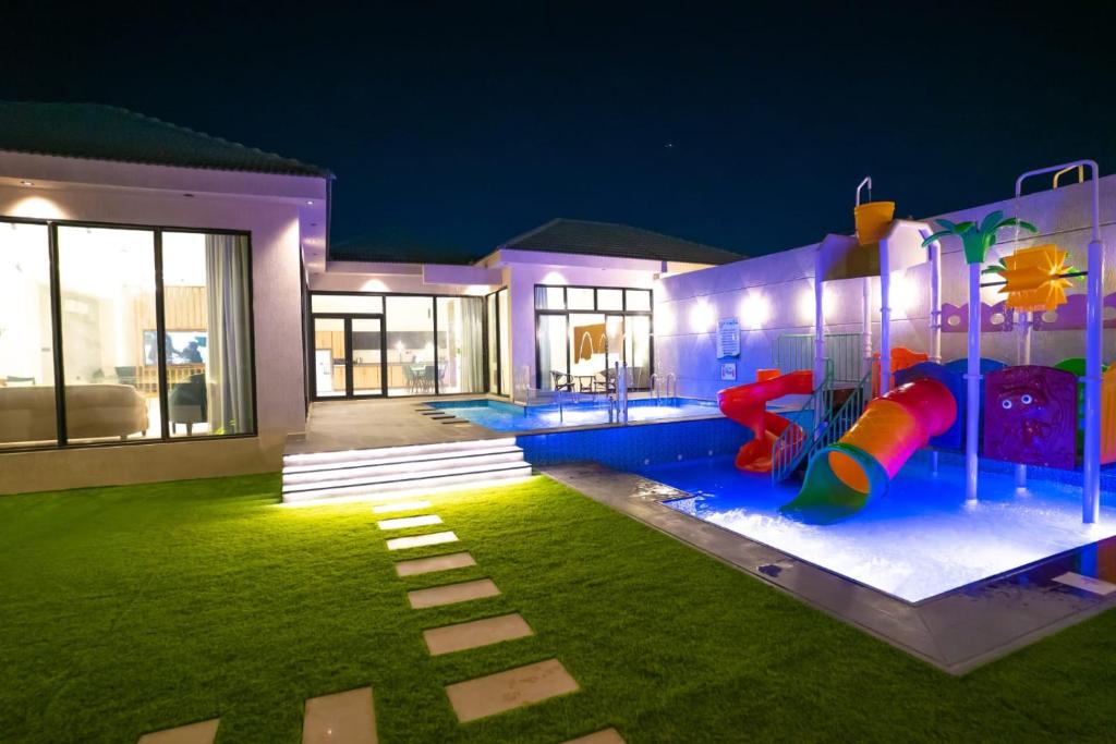 une maison avec une piscine avec un toboggan et une aire de jeux dans l'établissement شاليهات حكاية الفندفية, à Al Harazat