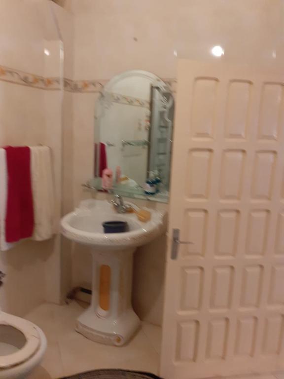 Baño blanco con lavabo y espejo en Bel Appartement à El kelaa Des Srarhna, en El Kelaa des Srarhna