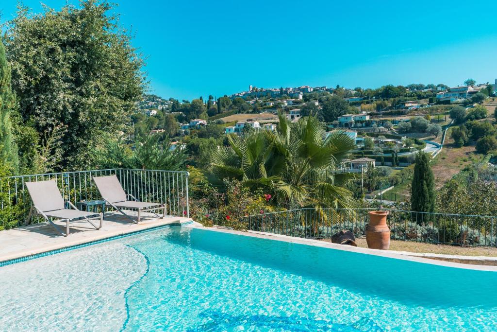 a pool with two chairs and a view of a city at Le Mas des Amandiers in Saint Paul de Vence