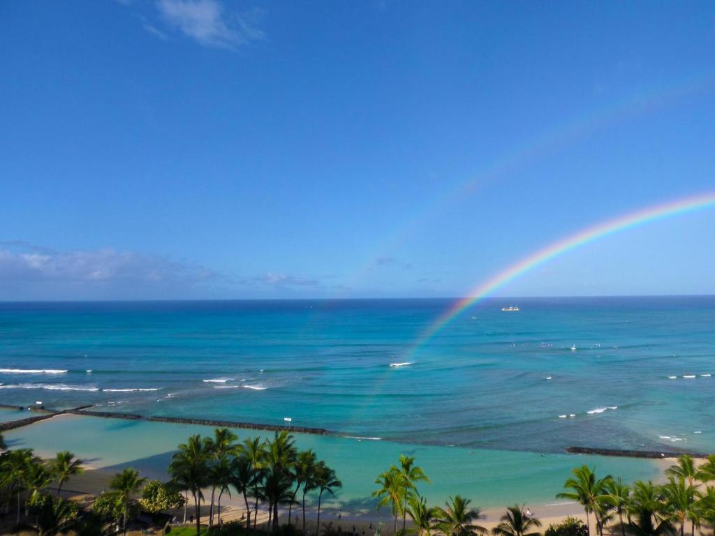 a rainbow over the ocean and a beach with palm trees at Waikiki Beach Tower in Honolulu