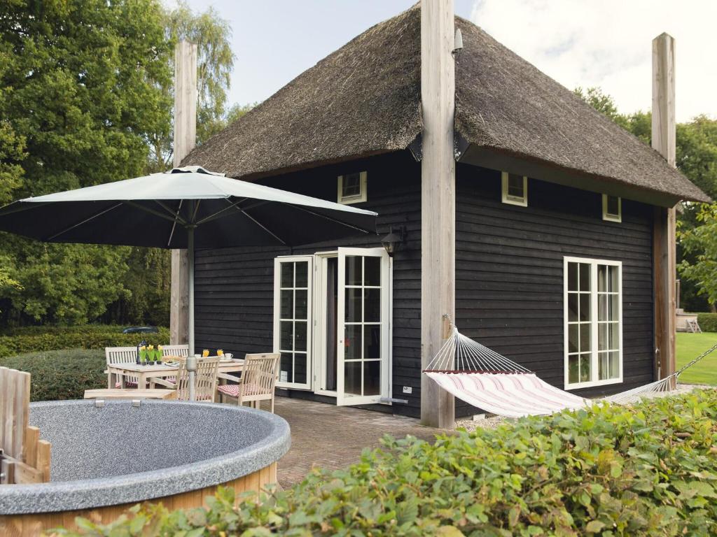 ein schwarzes Haus mit einem Sonnenschirm und Hängematten davor in der Unterkunft Cozy house with or without hot tub near a river in Notter