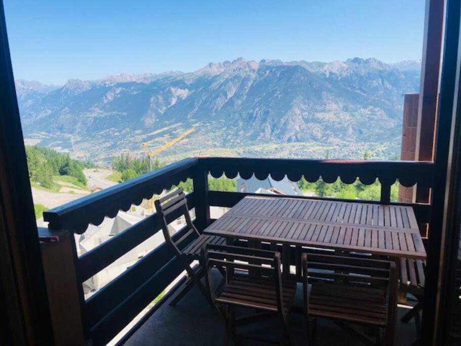 a wooden table and chairs on a balcony with mountains at Appartement risoul 1850 residence pegase in Risoul