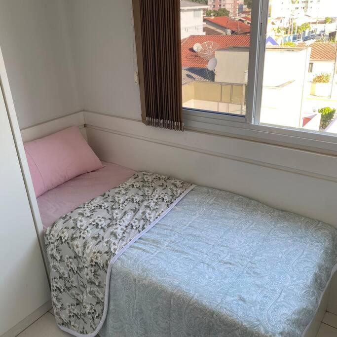 a small bed in a room with a window at Quarto solteiro em brusque in Brusque