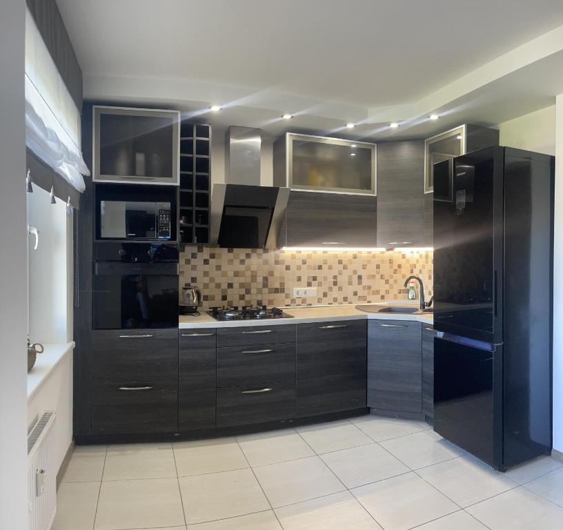 a kitchen with black cabinets and a black refrigerator at Suite Apartment in Šiauliai