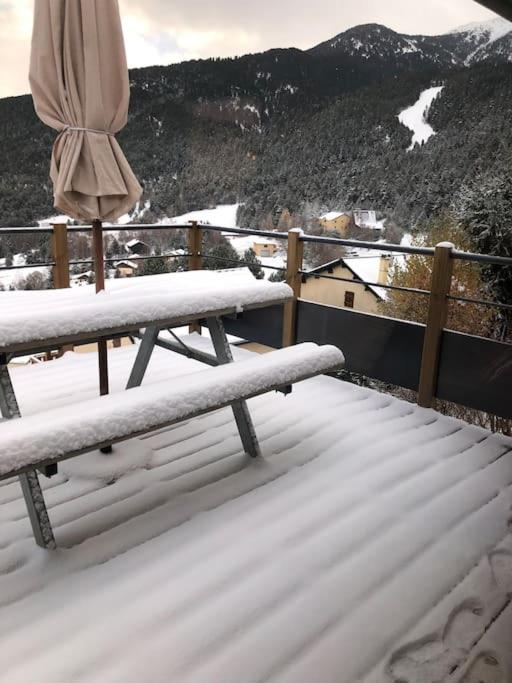 a snow covered bench on a balcony with a umbrella at Chalet au pied des pistes du Cambre d Aze in Saint-Pierre-dels-Forcats
