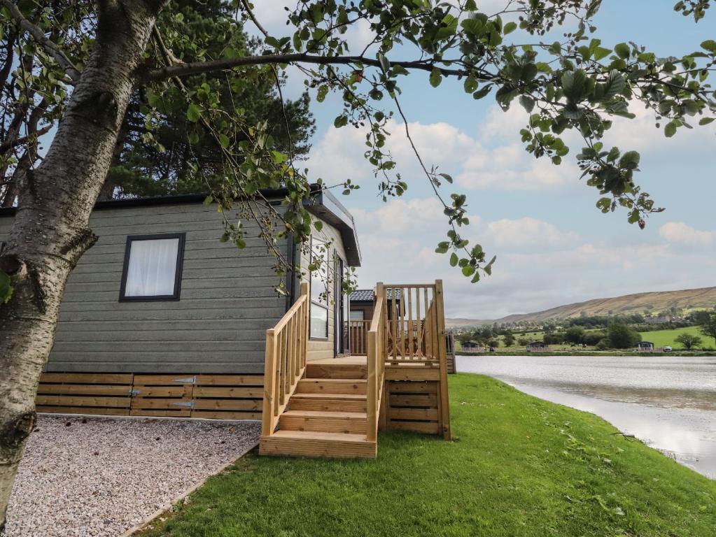 a tiny house with a porch and stairs next to a lake at Astoria Lodge in Clitheroe