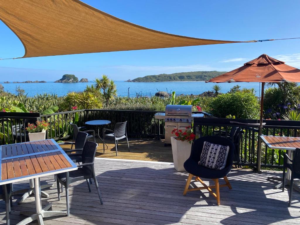 eine Terrasse mit Tischen, Stühlen und einem Sonnenschirm in der Unterkunft The Bay House Beachfront Accommodation in Cape Foulwind