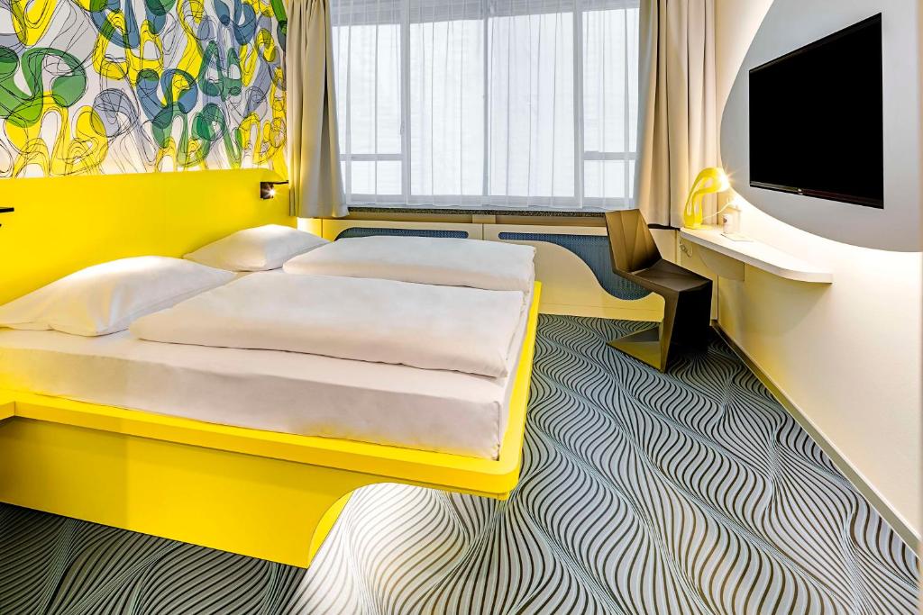 a yellow bedroom with a bed and a flat screen tv at prizeotel Dortmund-City in Dortmund