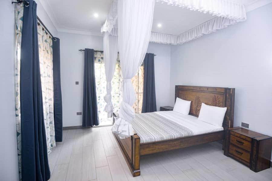 Schlafzimmer mit einem Bett mit weißer Bettwäsche und Vorhängen in der Unterkunft PearlCrest townhomes in Kampala