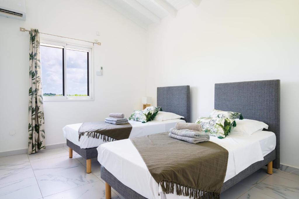 2 camas en una habitación blanca con ventana en Villa des Pentas – Chaleureuse Villa moderne avec piscine, en Baie-Mahault