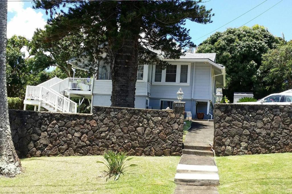 a white house with a stone wall and a tree at Cool, quiet ocean view 30 day min in Honolulu
