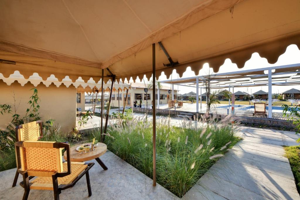 un patio con mesa, sillas y sombrillas en The Fern Seaside Luxurious Tent Resort Diu, en Diu