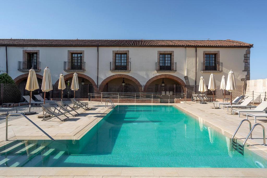 a pool with chairs and umbrellas in front of a building at Parador de Plasencia in Plasencia