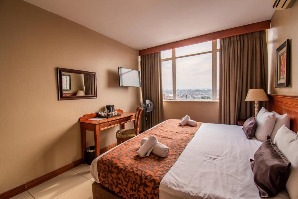 ダーバンにあるEmakhosini Hotel On Eastのベッド、デスク、窓が備わるホテルルームです。