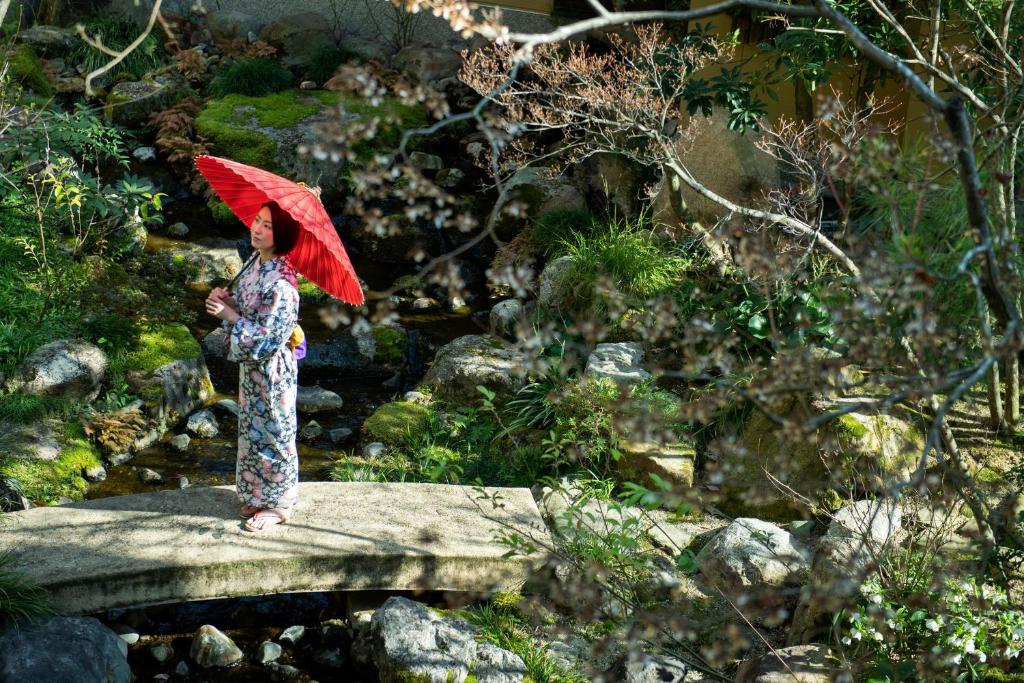a woman standing on a bridge with a red umbrella at Kifuno Sato in Mimasaka