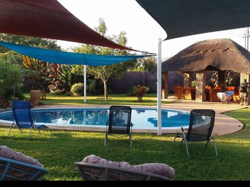 a yard with chairs and a swimming pool with an umbrella at Room in Villa - Zambezi Family Lodge - Rhino Room in Victoria Falls