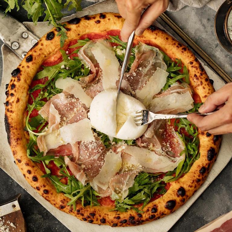 a person cutting a pizza with a fork and knife at The Reverie Saigon in Ho Chi Minh City