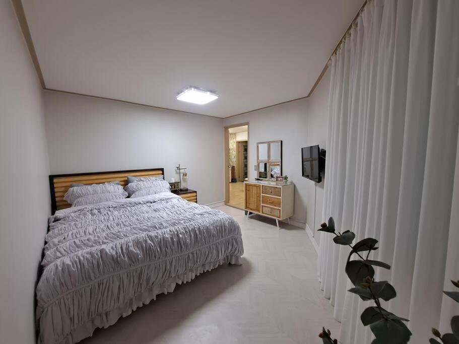 a white bedroom with a bed and a television at Dongpirang Purple House 2 in Tongyeong