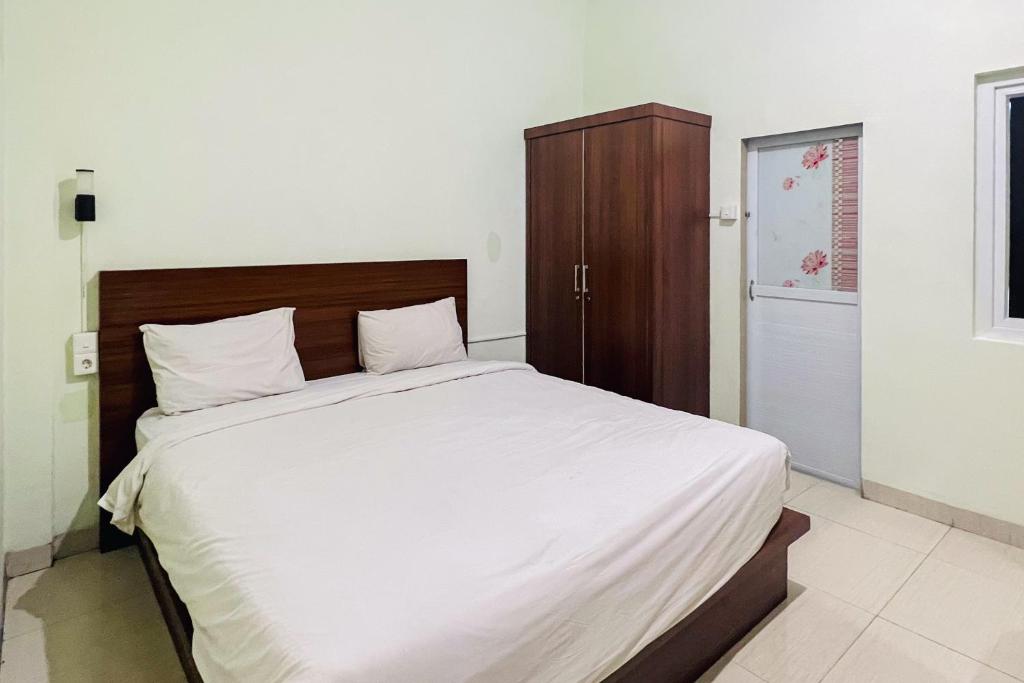 Schlafzimmer mit einem großen weißen Bett mit einem Kopfteil aus Holz in der Unterkunft Teratai Residence Mitra RedDoorz in Medan