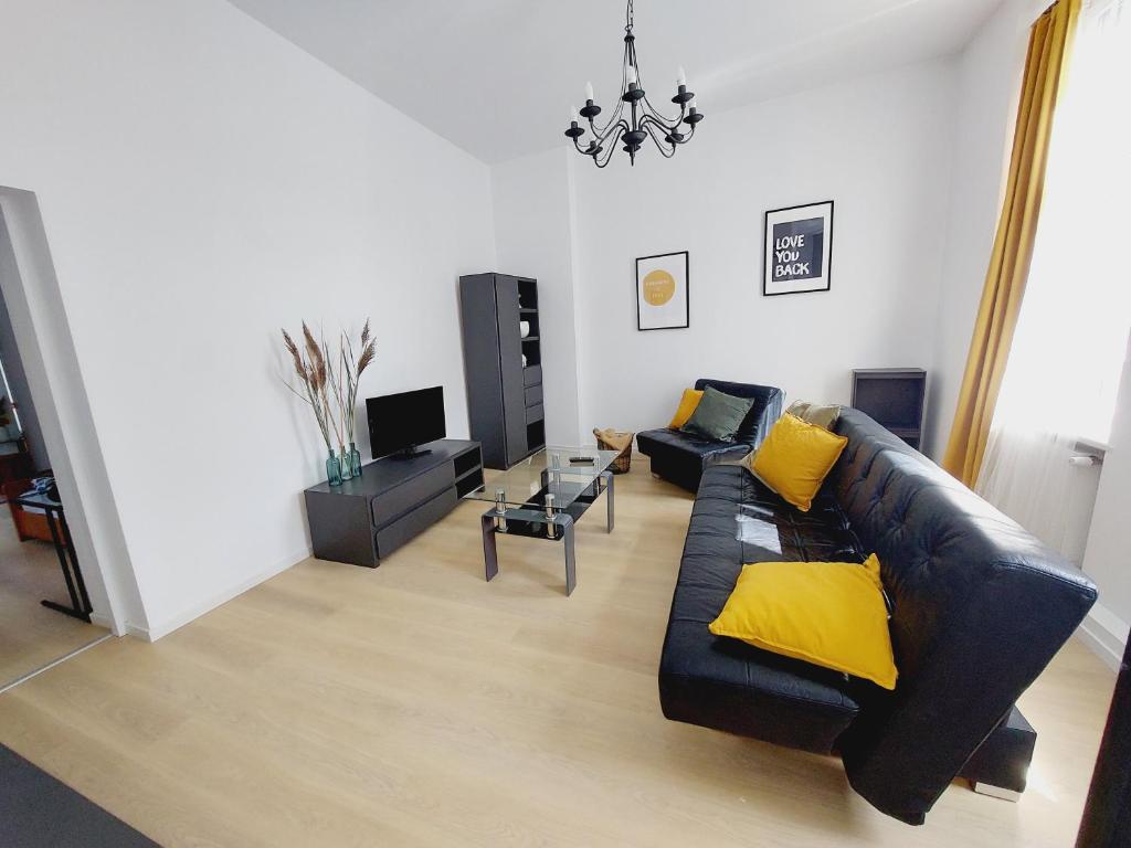 a living room with a black leather couch and yellow pillows at Apartament Aleja Przyjaźni in Gliwice