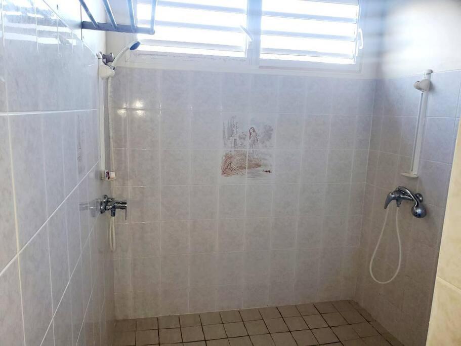 La salle de bains est pourvue d'une douche carrelée de blanc et d'une fenêtre. dans l'établissement petit paradis du thermaliste, à Lamentin