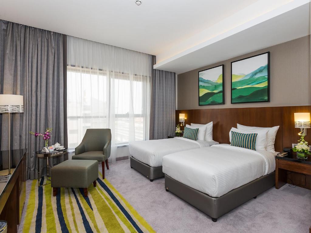 a hotel room with two beds and a chair at Flora Al Barsha Hotel At The Mall in Dubai