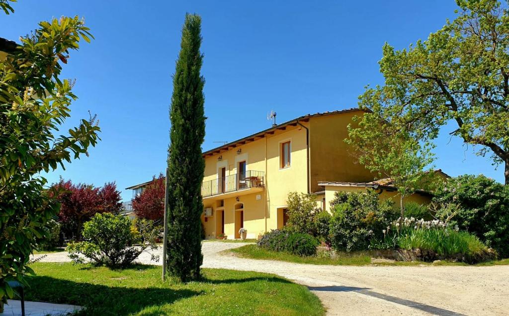 Una casa amarilla con un árbol delante. en Agriturismo Podere Casa al Vento, en Montepulciano