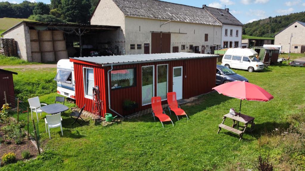 uma pequena casa vermelha com cadeiras, uma mesa e um guarda-sol em Tiny House Anneliese Hunde okay em Oberbettingen