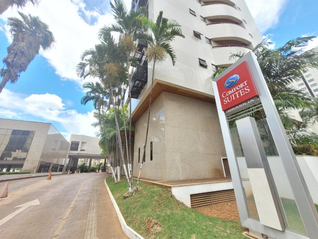 a sign in front of a building with palm trees at Comfort Suites By Rei dos Flats in Brasília