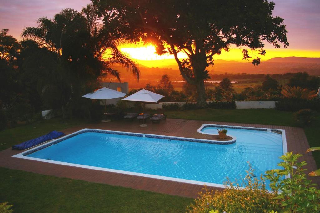 a swimming pool with a sunset in the background at Plumbago Guest House in Hazyview