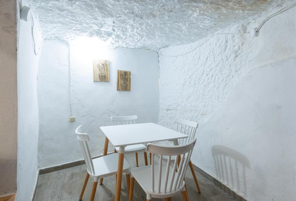 una mesa y sillas en una habitación con paredes blancas en Casa cueva El establo del Júcar, en Alcalá del Júcar