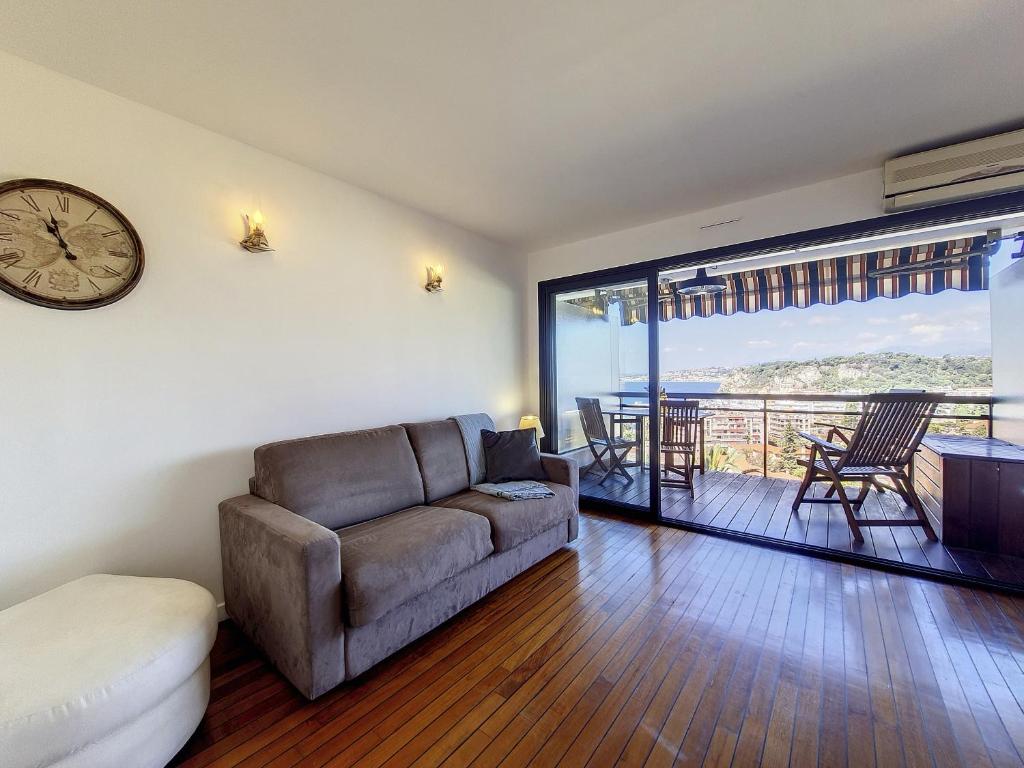 a living room with a couch and a clock on the wall at Nestor&amp;Jeeves - HUBLOT TERRASSE - Sea view - swimming pool in Nice